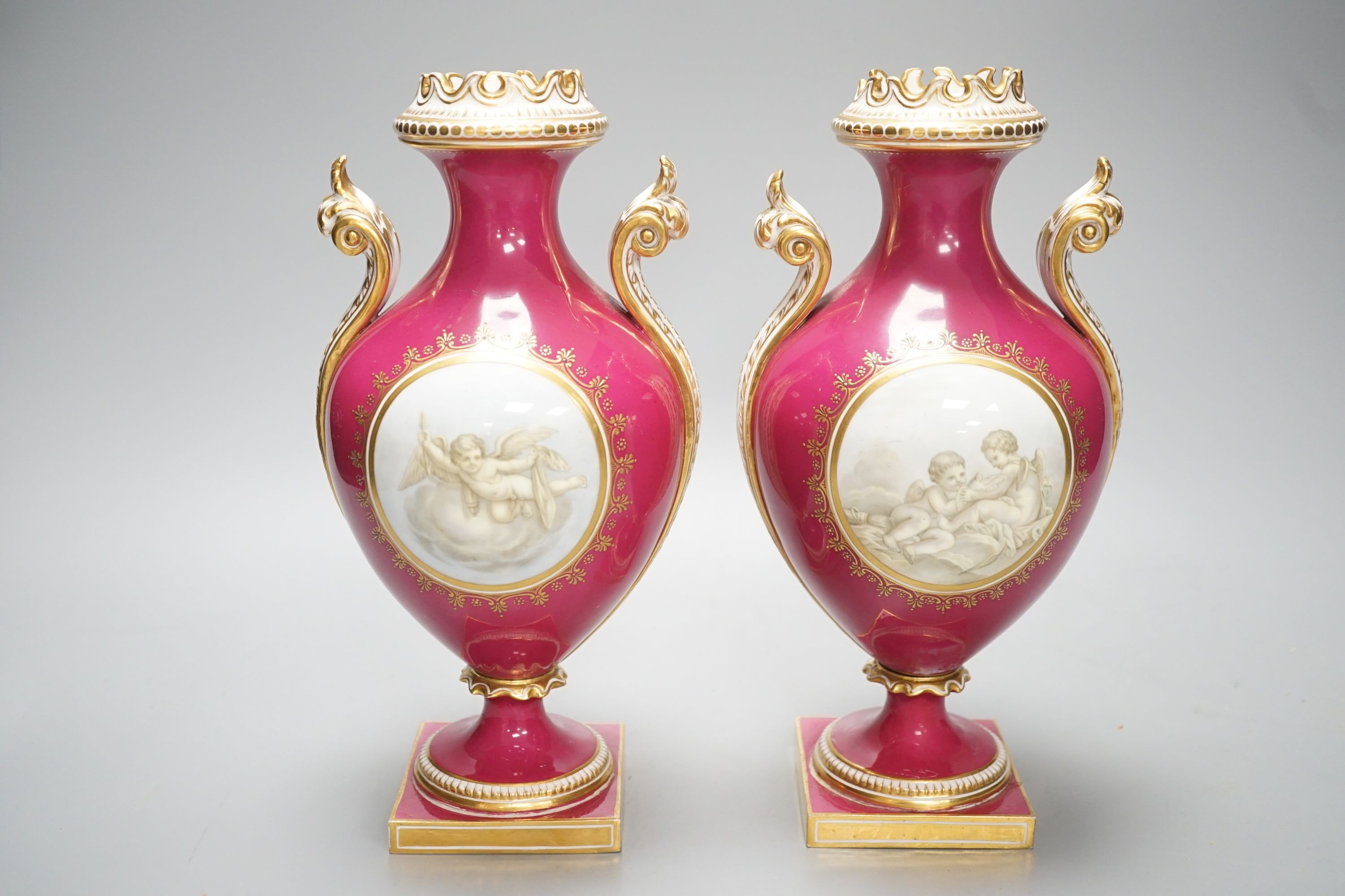 A pair of Coalport vases painted en-grisaille with cherubs in Chelsea style on a crimson ground, CSN mark in gold to one, height 23.5cm